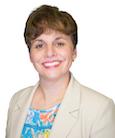 Headshot - Dark short haired woman in Tan suit Jacket and Pale Blue blouse