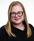 Headshot: Long Blonde haired woman with Glasses and black Suit jacket and blue top smiling at the camera.